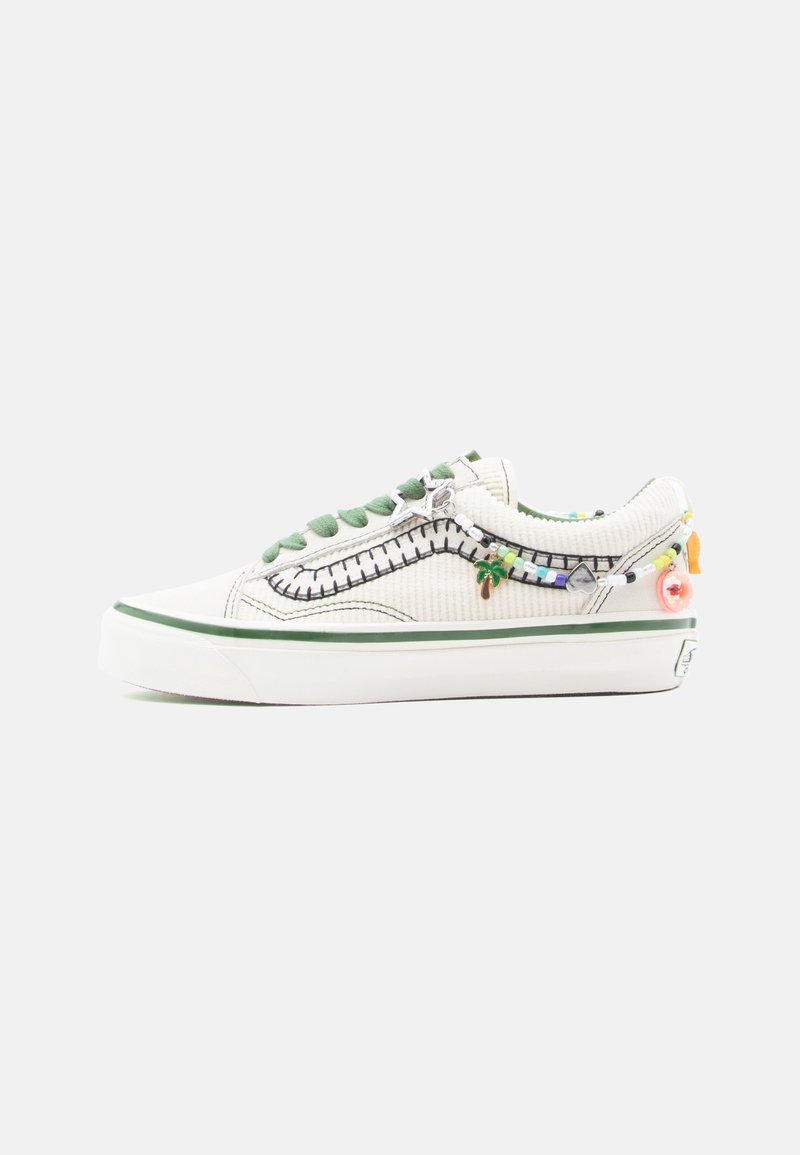 Baskets basses blanches avec des accents verts, des lacets verts, des détails de couture noirs et une chaîne de charms colorés en perles le long du côté.