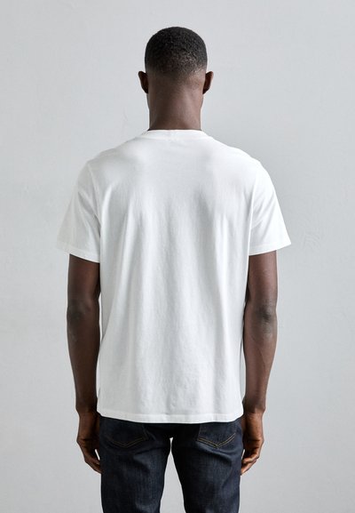T-shirt en coton blanc avec un col rond, des manches courtes et une coupe décontractée, associé à un jean bleu foncé. Design sans couture avec aucun motif visible.