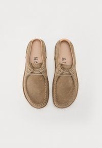 Scarpe in suede marrone con punta arrotondata, dettagli in pizzo e cuciture a contrasto. La soletta è beige con il marchio.