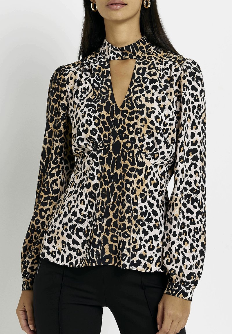 Blouse en imprimé léopard avec un col haut, un décolleté en forme de clé, des manches longues et une texture soyeuse. Fond neutre.