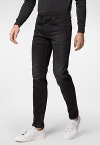 Svart denimjeans med slim passform, midjeresnitt, framfickor och subtila sömdetaljer, kombinerade med vita sneakers.