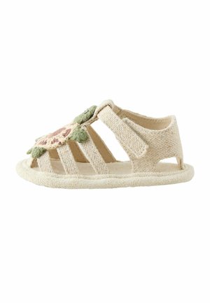 Beige Kleinkind-Sandale mit weichen Stoffriemen, einem Klettverschluss und einer rosa-grünen Blumenapplikation obenauf.