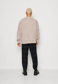 Sudadera oversized de color beige claro con puños acanalados, combinada con pantalones a cuadros azul oscuro. Unos zapatos negro gruesos completan el conjunto.