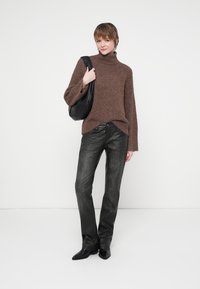 Pull en maille brun à col roulé avec des manches oversize, associé à un jean sombre et texturé. Sac en cuir noir porté à l'épaule.