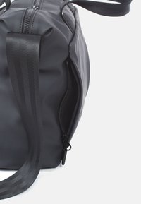 Schwarze Sporttasche mit glattem, wasserdichtem Außenmaterial, Reißverschluss und doppelten Stoffgriffen für einfaches Tragen. Verfügt über ein minimalistische Design.