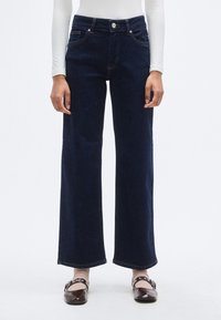 Σκούρο μπλε τζιν παντελόνι με φαρδιά γραμμή και ψηλή μέση, πέντε τσέπες και ασημένιες λεπτομέρειες. Διαθέτει λεία υφή τζιν και ίσια, ρέουσα σιλουέτα.