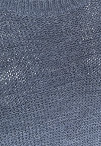 Framifrån av ett blått stickat tyg, med ett mönster med textur och öppna vävningar samt en ribbad krage. Mjukt, lätt material.