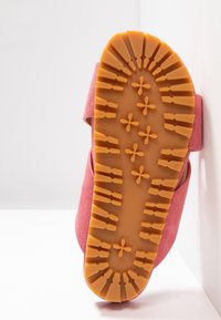 Sandale en suede rose avec une semelle en caoutchouc texturé couleur tan présentant un design de grip à motifs. Dos ouvert et sangle ajustable pour un maintien sûr.