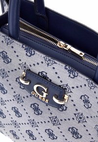 Borsa a mano in tessuto navy con motivo intricato, hardware dorato e dettaglio del logo. Presenta una chiusura a zip e doppie maniglie per il trasporto.