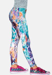 Kolorowe legginsy w odcieniach teal, pomarańczu i fioletu z błyszczącym wykończeniem. Do tego różowe trampki ozdobione wzorami i ozdobnikami.