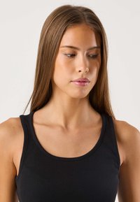 Zwarte geribbelde tanktop met een ronde halslijn en dunne bandjes, met een aansluitende pasvorm en een zachte textuur. Het haar valt recht en glad.