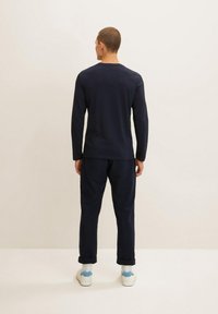 Camisa de manga larga azul marino con cuello redondo, combinada con pantalones a juego. Acentuada con calcetines blancos y zapatos de color azul claro.