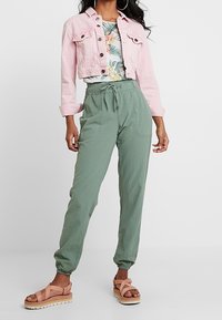 Veste en jean rose raccourcie, T-shirt à fleurs, pantalon vert ample et sandales à plateforme couleur beige. Textures douces, avec poignets et taille élastiqués.