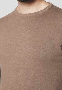 Pull en tricot marron avec un col rond, présentant une texture lisse et une coupe ajustée, mettant en valeur la conception du tissu sans couture.