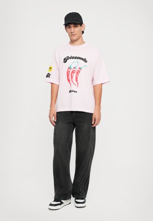 Pink short-sleeve t-shirt with red chili pepper graphic, paired with loose black jeans featuring side stitching and contrasting white sneakers.