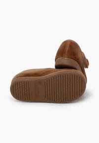 Zapatos de ante marrón con puntera redondeada y suela de goma texturizada; cuentan con un botón decorativo en el costado. Diseño estilo zapatilla.