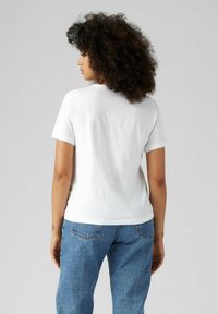 Camiseta de algodón blanca con mangas cortas, escote redondeado y forma ajustada. Combinada con jeans de mezclilla azul claro con bolsillos traseros.