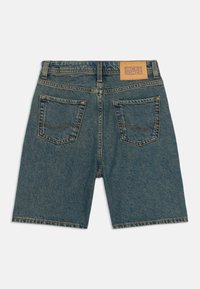 Pantalones cortos de mezclilla en azul medio, con una cinturilla y una etiqueta de cuero de marca. Dos bolsillos traseros con detalles de costura amarilla.