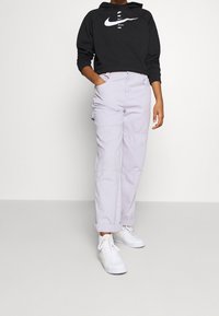 Schwarzer Baumwoll-Hoodie mit weißem Nike-Logo, kombiniert mit helllila weiten Cargo-Hosen und weißen Sneakern. Schlichtes, funktionales Design.