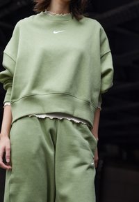 Zelená zkrácená mikina a odpovídající kalhoty z jemného materiálu, s bílým logem Nike a nařaseným lemem pod tričkem.