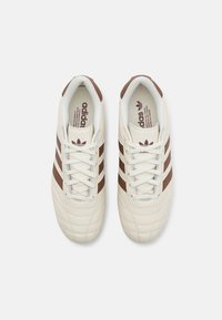 Adidas-sneakers med krämfärgat läderöverdel, bruna ränder, texturerade detaljer och snörning. Märkt innersula.