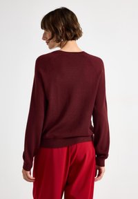 Burgundin neulepaita, jossa on pitkät hihat ja ribbireuna. Pehmeä rakenne ja rento istuvuus, yhdistettynä kirkkaanpunaisiin housuihin.