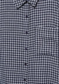 Camicia a quadri blu navy con motivi a rete bianca e azzurri chiari, colletto e taschino sul lato sinistro del petto.