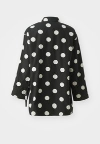 Chemise noire à pois blancs, dotée d'un col et de manches longues avec détails aux poignets, en tissu léger.