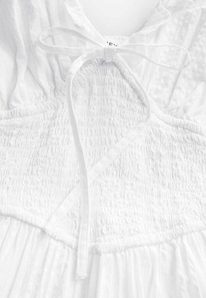 Robe blanche avec un corsage smocké, un détail à nouer au cou et une jupe fluide en tissu texturé.
