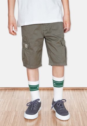 Olijfgroene cargoshorts met zijzakken en een relaxed fit, gecombineerd met witte sokken en grijze sneakers. Verticaal gestreepte sokken.