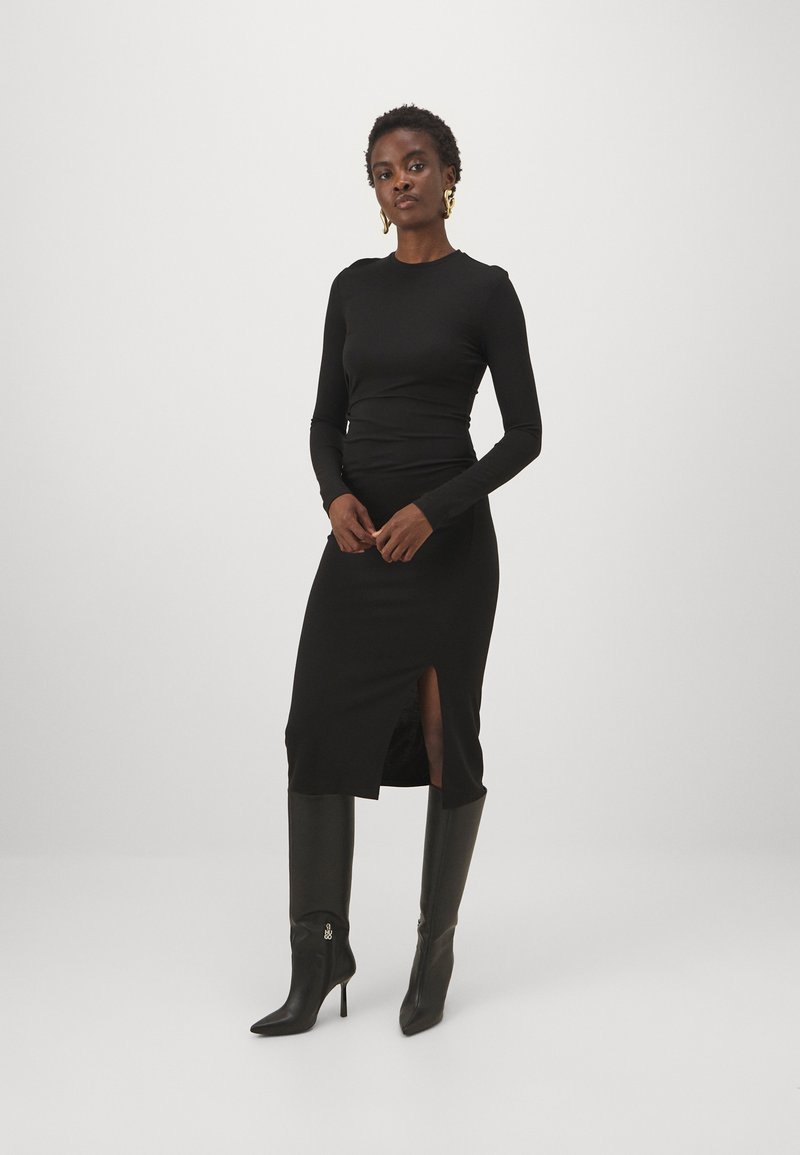 Melnas garās piedurknes kleitas ar pieguļošu augšu un sānu šķēlumu, kombinēta ar melniem augstiem apkaklīšu zābakiem. Gluda auduma, minimālistisks dizains.