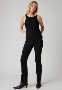 Jeans ajustados negros de mezclilla con una textura suave, combinados con una blusa sin mangas negra y botines de punta. Diseño simple.