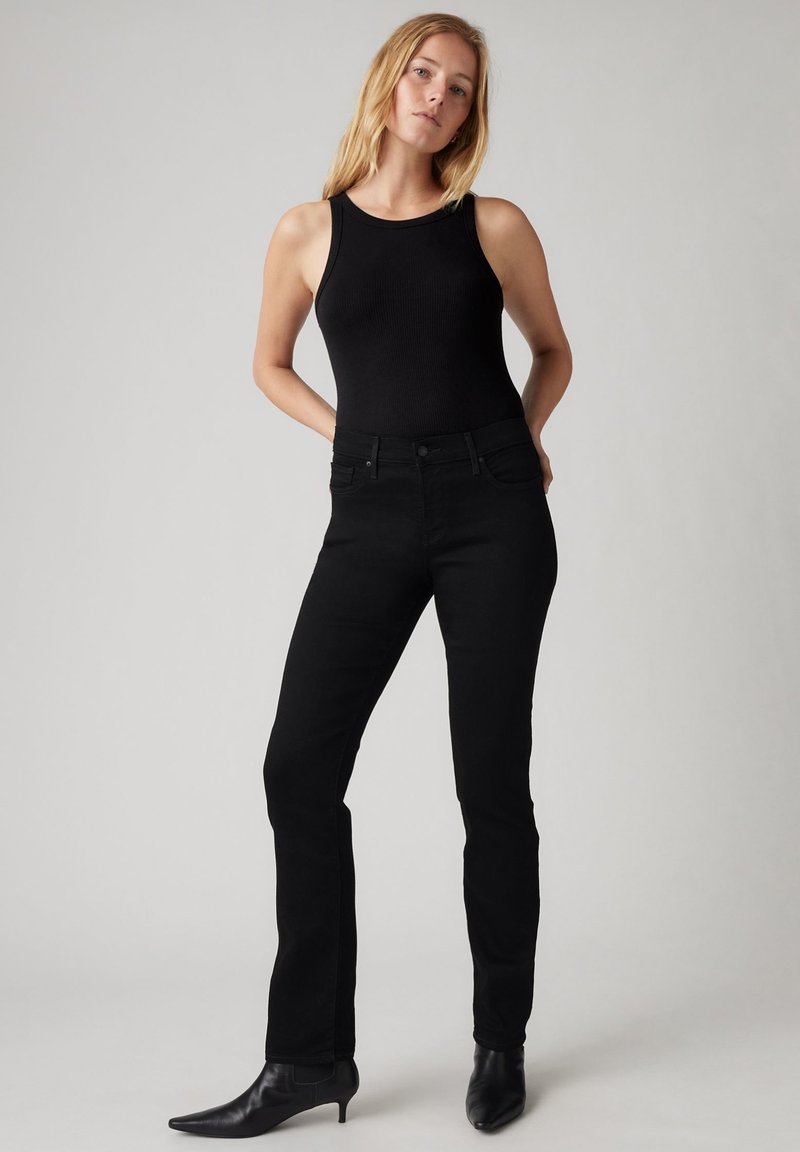 Jeans ajustados negros de mezclilla con una textura suave, combinados con una blusa sin mangas negra y botines de punta. Diseño simple.
