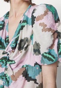 Primer plano de un vestido con mangas abullonadas que presenta patrones florales abstractos en colores verde, rosa, marrón y verde azulado sobre una tela clara.