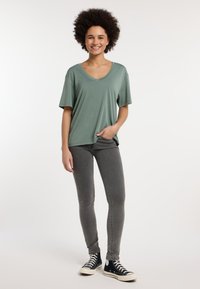 T-shirt verde chiaro a maniche corte con scollo a V e spacco laterale, abbinato a jeans skinny grigi e sneakers nere alte. Texture liscia in tutto il capo.