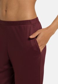 Bordeauxfärgade byxor med elastisk midja, utrustade med en sidficka. Tyget ser slätt och lätt ut, perfekt för komfort och rörelse.