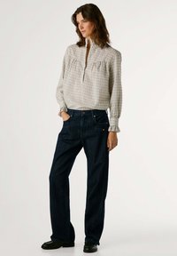 Blusa de cuadros grises con media cremallera, detalles fruncidos, combinada con pantalones vaqueros de pierna ancha en azul oscuro y zapatos negros.
