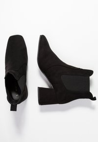 Botines negros de ante con puntera afilada, paneles laterales elásticos y un tacón cuadrado. Presentan una pestaña trasera para facilitar su uso.