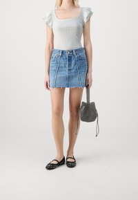 Light gray short-sleeve bodysuit, denim mini skirt with frayed hem, black studded flats, and a small patterned bucket bag.