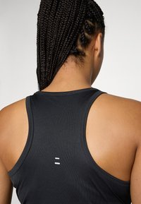Zwarte sportieve tanktop met een racerback ontwerp, voorzien van een subtiele witte logodetail op de rug, gemaakt van een gladde, rekbare stof.