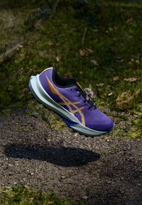 Purple trail running shoe with black accents, featuring a textured upper, gold logo, and a white midsole suitable for uneven terrain.