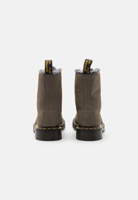 Brune skinn ankle støvler med en teksturert overflate, grå pelsfôr og svarte gummisåler. Kjennetegnes av gule stikninger og pull tabs.