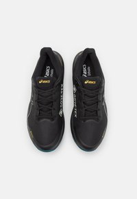 Černé sportovní boty s texturovaným textilním svrškem, s označením GORE-TEX a bílými akcenty. Mají šněrovací design a polstrovanou podrážku.
