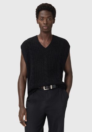 Black sleeveless knit top with a V-neck, featuring textured ribbing. Paired with black trousers and a silver-buckled belt.
