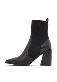 Bottine noire en cuir lisse et tissu côtelé, dotée d'un bout pointu et d'un talon épais pour la stabilité.