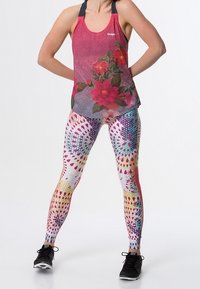 Top senza maniche rosso con motivo floreale e spalline nere, abbinato a leggings colorati a spirale che presentano una combinazione di rosa, blu e giallo. Sneakers nere.