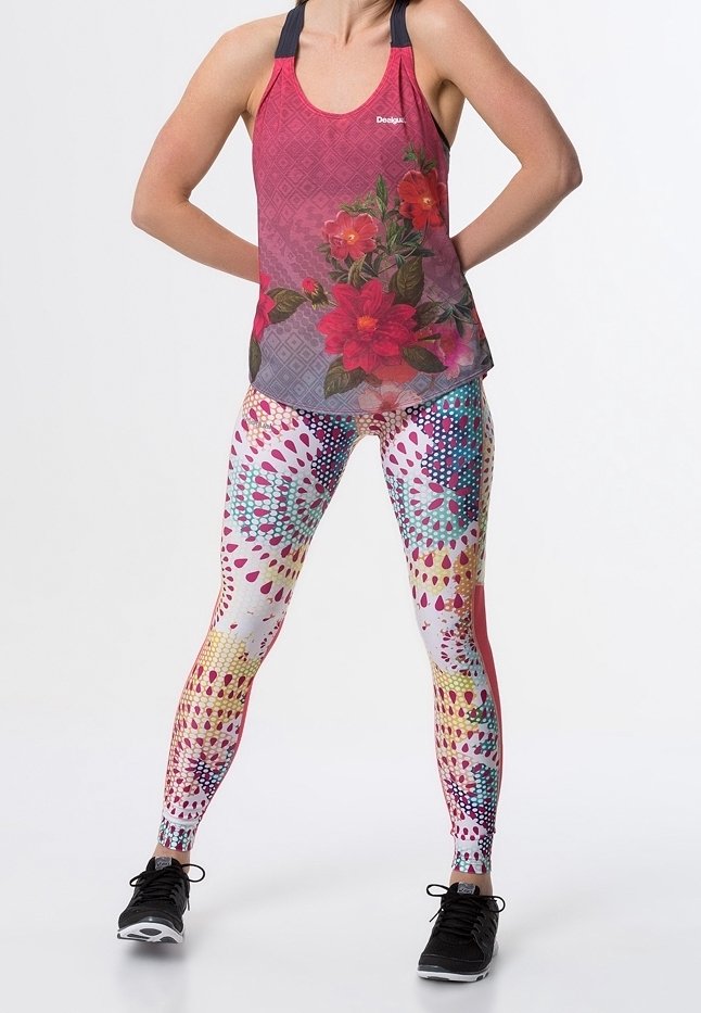 Top senza maniche rosso con motivo floreale e spalline nere, abbinato a leggings colorati a spirale che presentano una combinazione di rosa, blu e giallo. Sneakers nere.