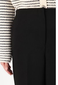 Calças pretas ajustadas com uma textura suave. Combinadas com uma blusa de malha com padrão riscas, apresentando riscas pretas e brancas, decorada com um detalhe de botão.