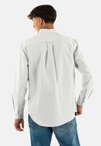 Camicia a righe blu chiaro e bianche con una piega sul retro, polsini con bottone e colletto a punta. Realizzata in tessuto leggero con una texture liscia.