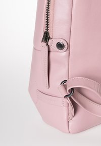 Borsa in pelle rosa con una texture liscia, dotata di chiusura con zip e un dettaglio in metallo nero. Include un'etichetta in pelle con il marchio e angoli arrotondati.